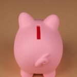 pexels-photo-11933551-11933551 Pink piggy bank standing on a neutral brown surface, captured in a minimalist style.